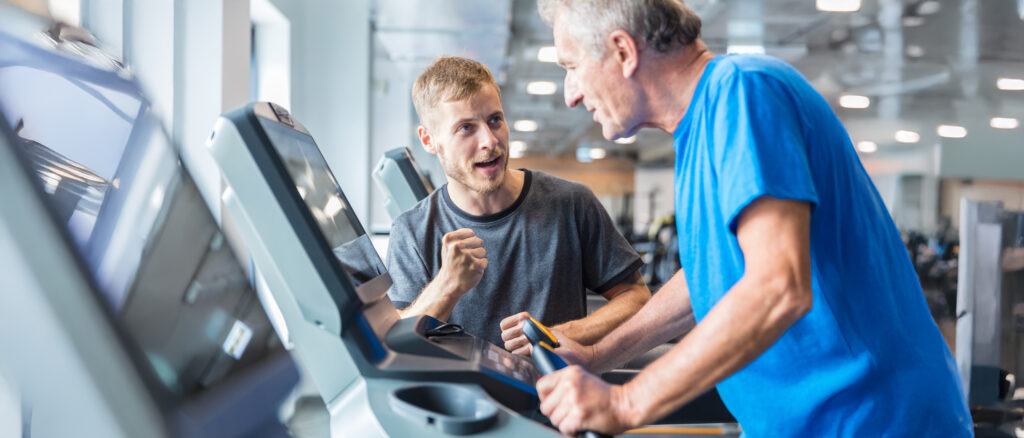 Trainer motivating senior man walking on treadmill